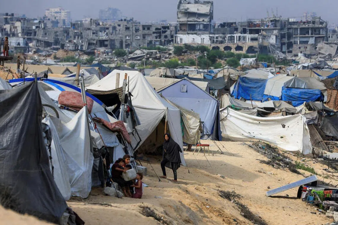 Displaced Palestinians shelter in a tent camp as buildings damaged during the Israeli offensive appear in the background, in the northern Gaza Strip August 10, 2025. REUTERS/Dawoud Abu Alkas