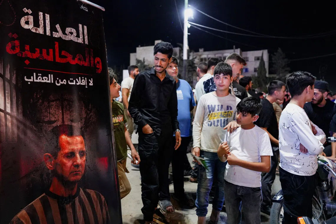 People gather beside a poster depicting ousted President Bashar al-Assad as Syrians celebrate after a Syrian court sentenced Assad and officials who served under his rule to death, in Idlib, Syria, August 11, 2026. REUTERS/Karam al-Masri