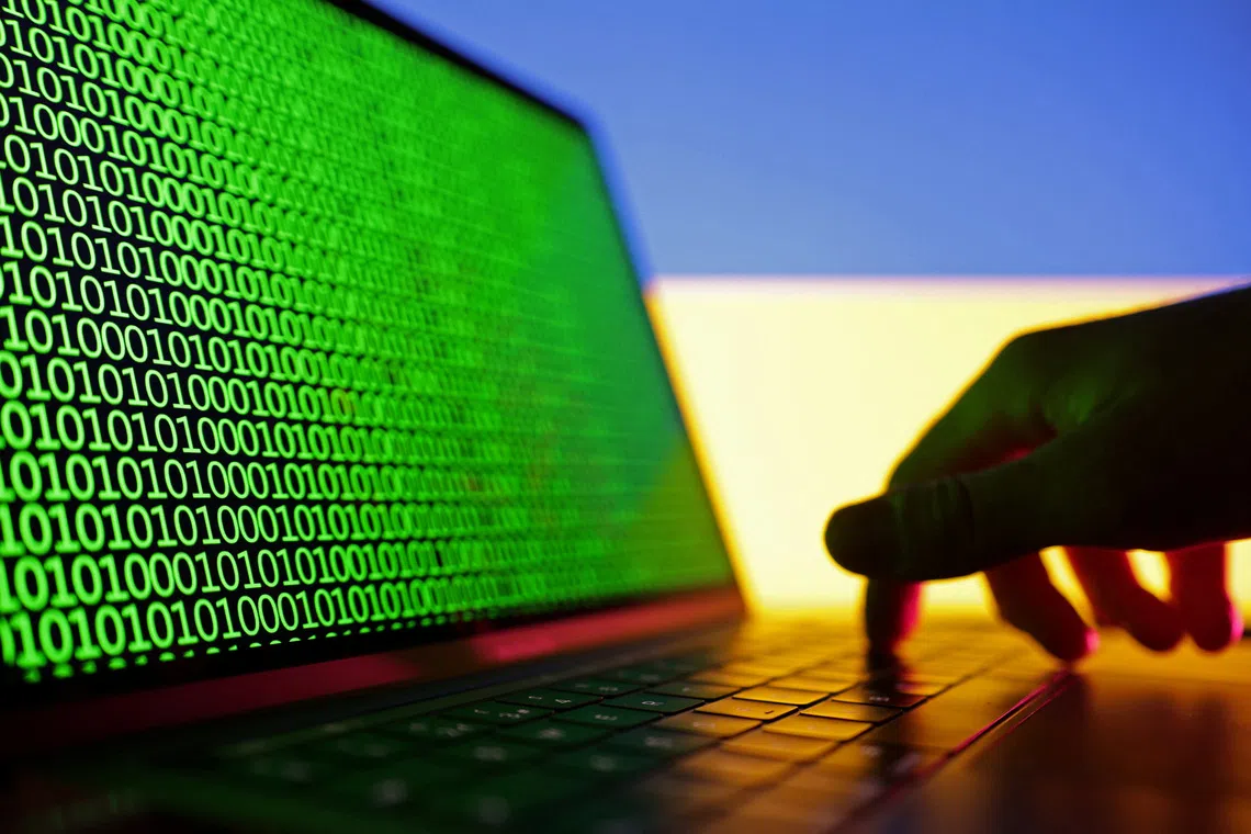 A hand is seen on a laptop with binary codes displayed in front of the Ukrainian flag in this illustration taken, August 19, 2022. REUTERS/Dado Ruvic/Illustration