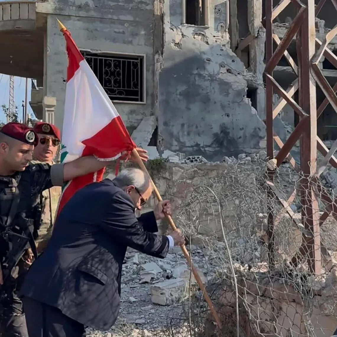 Lebanese Prime Minister Nawaf Salam placing a national flag along a damaged street in the southern village of Zawtar al-Gharbiya on July 22.