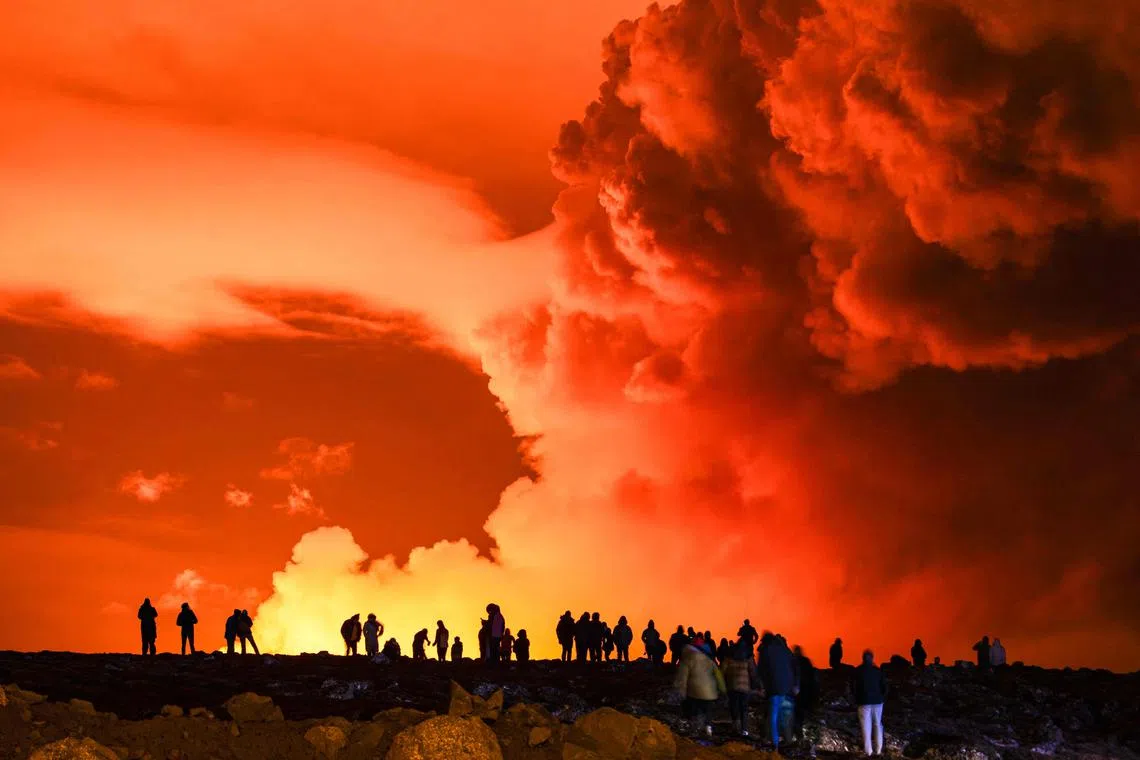 People gather to watch as molten lava flows out from a fissure on the Reykjanes peninsula, in Iceland.