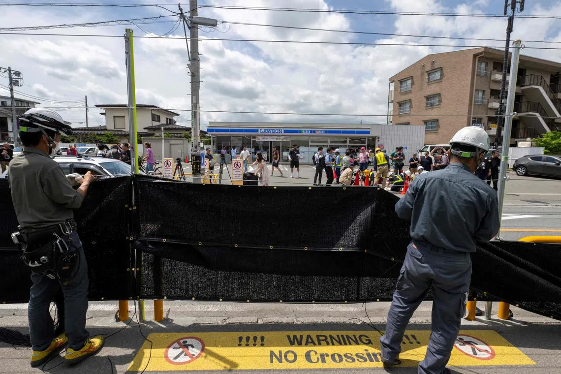 Workers install a barrier to block the sight of Japan's Mount Fuji emerging from behind a convenience store to deter badly behaved tourists, in the town of Fujikawaguchiko, Yamanashi prefecture on May 21, 2024. The plan to erect a large mesh barrier across the road from an Instagram-famous view of Mount Fuji made headlines last month when it was announced by officials fed up with what locals said were unending streams of mostly foreign visitors littering, trespassing and breaking traffic rules. (Photo by Kazuhiro NOGI / AFP)
