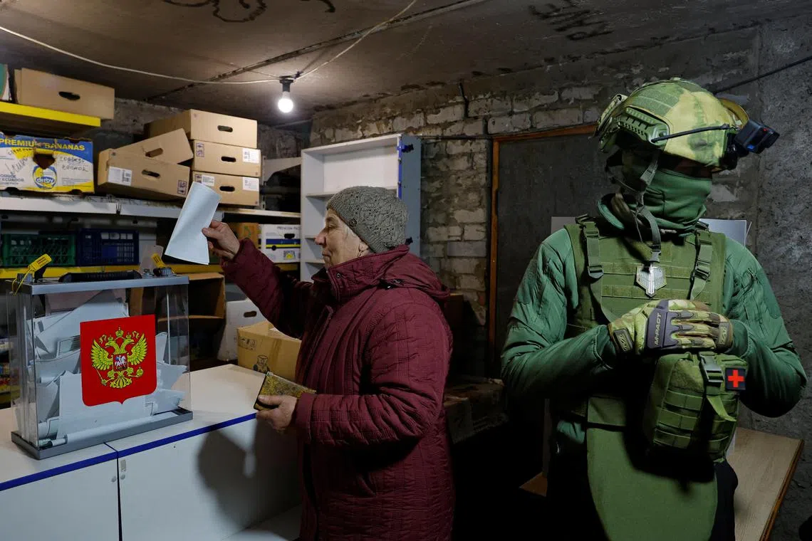 A resident puts her voting paper into a mobile ballot box, in the basement of a destroyed apartment building in Russian-controlled Avdiivka, in Ukraine's Donetsk region.