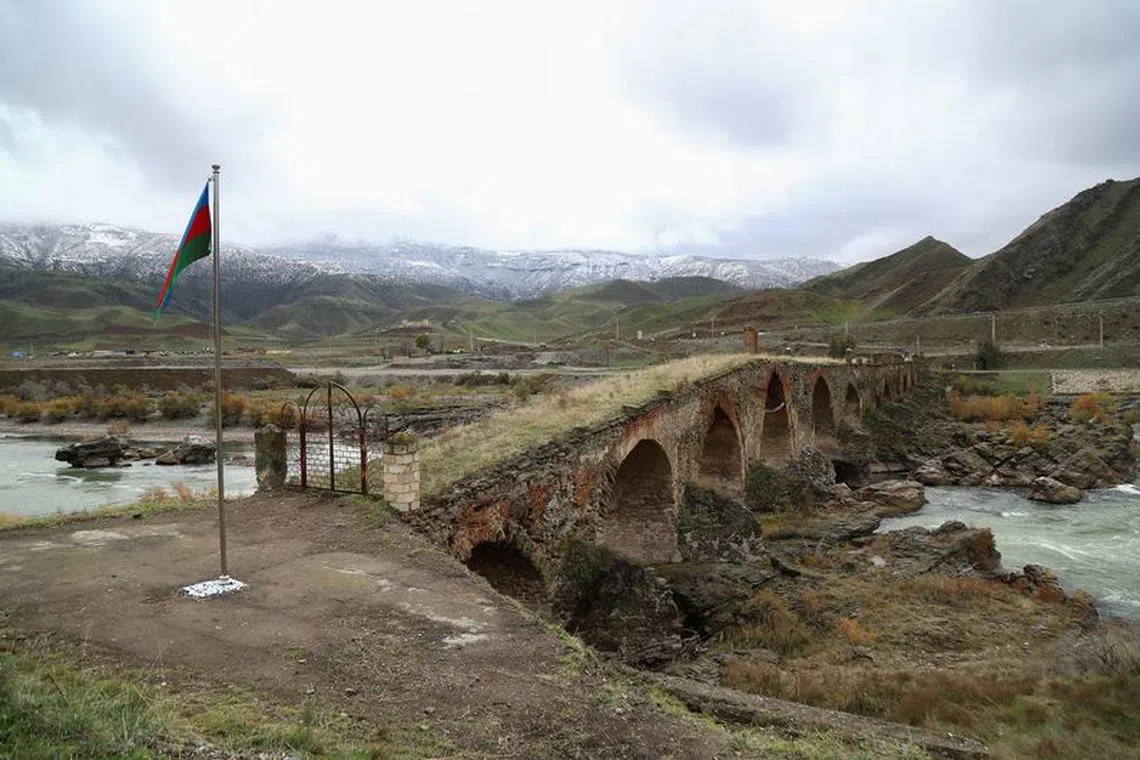 An Azerbaijani national flag is seen next to the ancient Khodaafarin Bridge near the border with Iran in the area, which came under the control of Azerbaijan's troops following a military conflict over Nagorno-Karabakh against ethnic Armenian forces and a further signing of a ceasefire deal, in Jabrayil District, December 7, 2020. Picture taken December 7, 2020. REUTERS/Aziz Karimov/File Photo