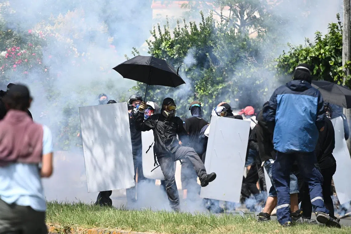 A demonstrator throws back a tear gas canister at riot police.