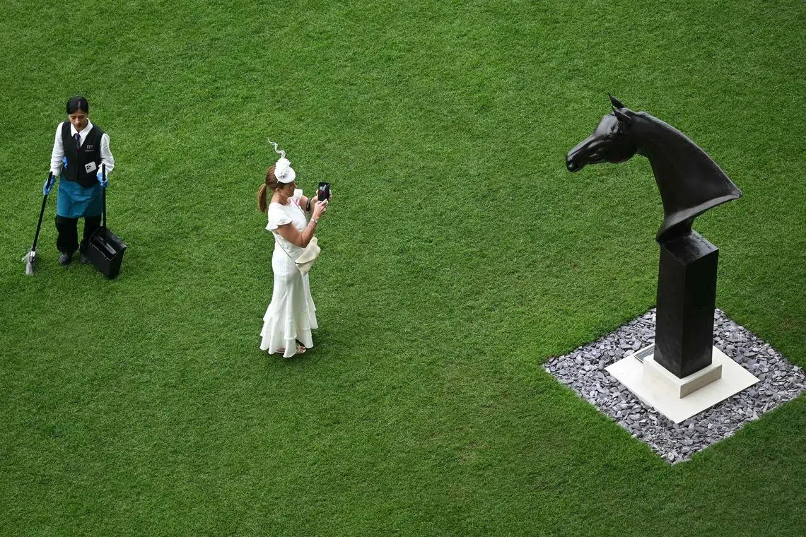 A racegoer taking a picture of a statue of the horse 'Enable', as they attend the third day of the Royal Ascot horse racing meeting in Ascot, west of London, on June 18, 2026. 