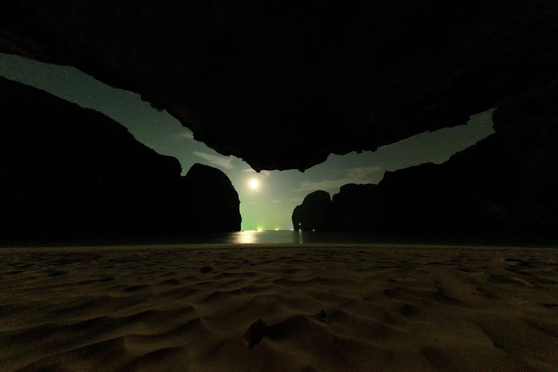 The moon is seen from inside a cave in Maya Bay at the Phi Phi Island National Park, on Phi Phi Leh Island on Feb 27, 2023. The green light pollution on the horizon is from squid fishing boats. A number of factors affect the sharks around Phi Phi Leh Island, including seasonal movement patterns and human activity like fishing. 