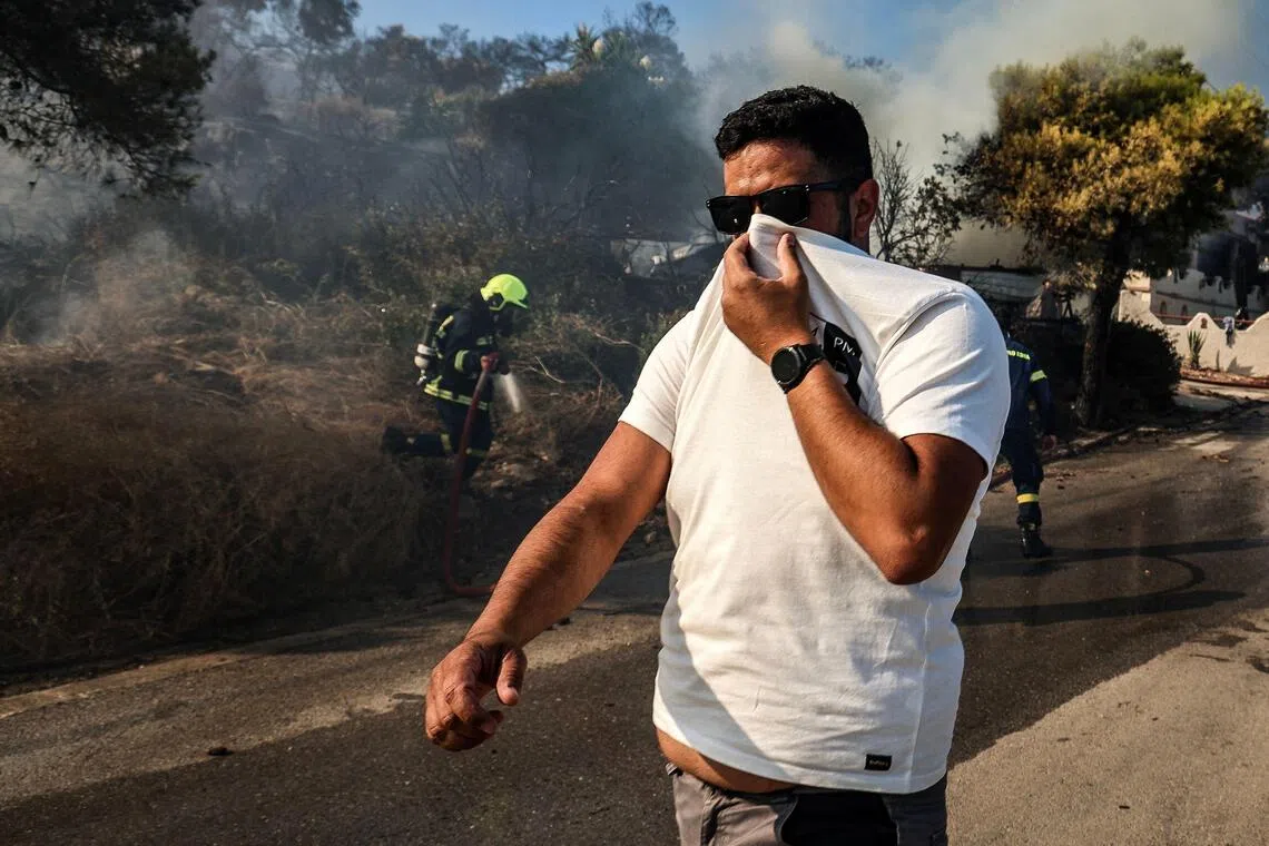 A man covering his face from the smoke as firefighters tackle a wildfire on the island of Salamina, near Athens, on Aug 16.