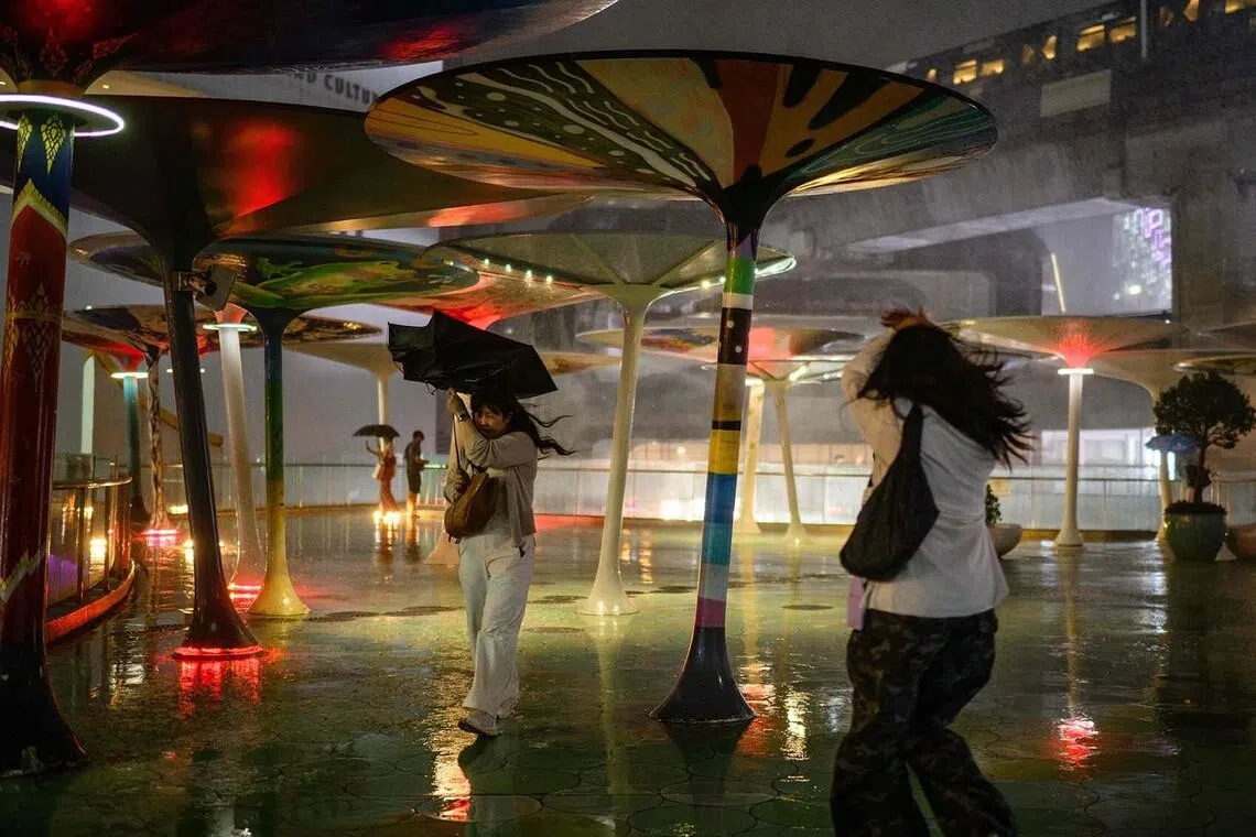 TOPSHOT - A woman uses an umbrella to shield herself from the rain during a heavy downpour in Bangkok on July 8, 2026. (Photo by Anthony WALLACE / AFP)