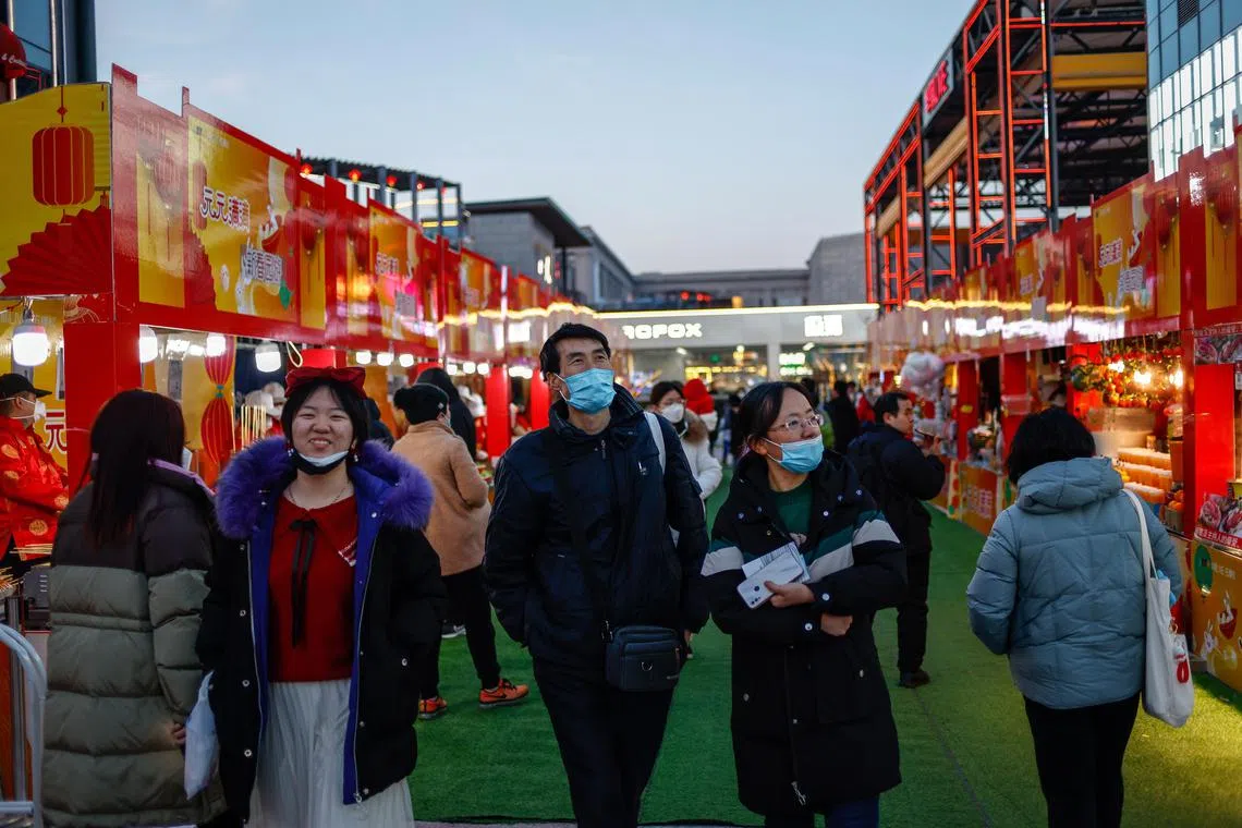 People walk along food stalls at a shopping district in Beijing on Feb 3, 2023.