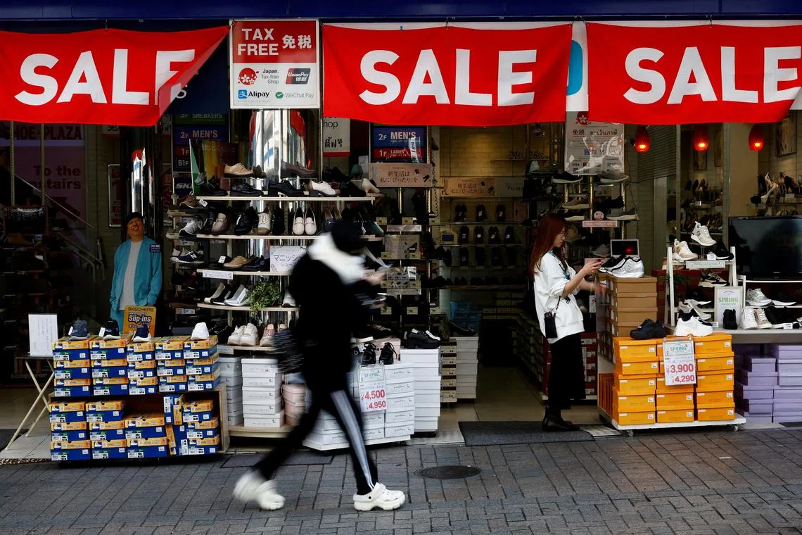 FILE PHOTO: A passerby walks past a retail shop displaying 'SALE' banners in Tokyo, Japan February 15, 2024.  REUTERS/Issei Kato/File Photo