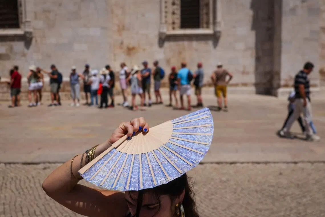 A woman shading her head with a fan in front of Jeronimos Monastery in Belem, during a heatwave in Lisbon, on May 27, 2026. 