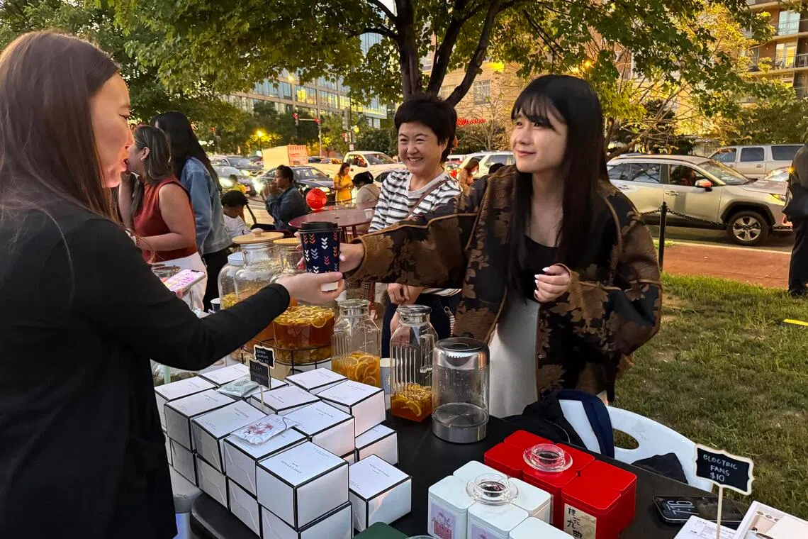 Zhu Simin (right), who was born in China and moved to the US, tending to her Chinese tea booth at the Mid-Autumn Festival night market at Washington, DC’s Chinatown Park in September.