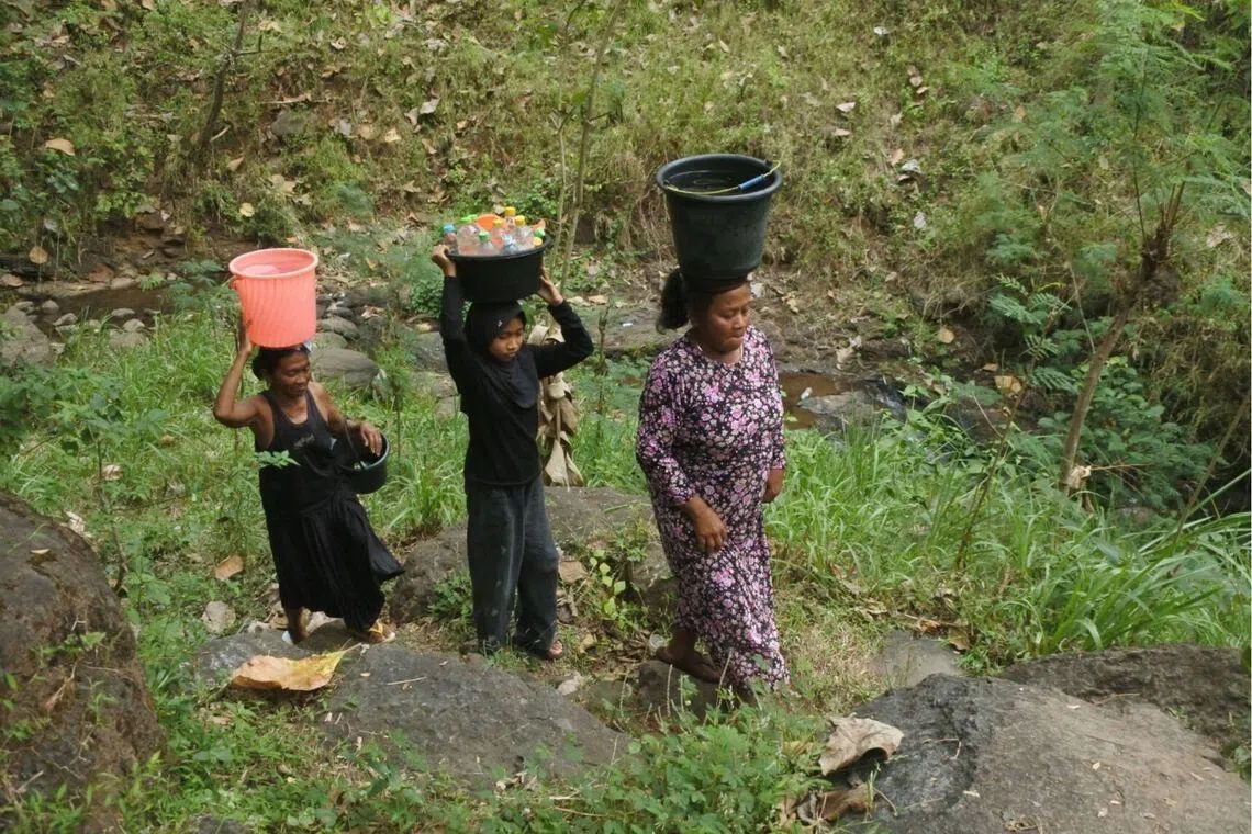 Residents carry buckets of water collected from a natural spring on June 20 in East Java. Villagers say they have struggled to access clean water for drinking and daily needs over the past month, forcing them to walk about 1km to the spring.