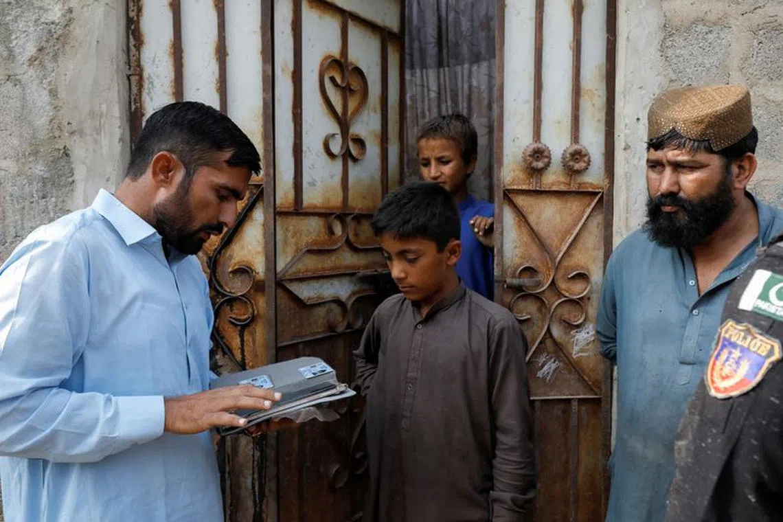 A worker from the National Database and Registration Authority (NADRA), speaks to residents while verifying their identity cards on an online tab, during a door to door search and verification drive for undocumented Afghan nationals, in an Afghan Camp on the outskirts of Karachi, Pakistan, November 21, 2023. REUTERS/Akhtar Soomro