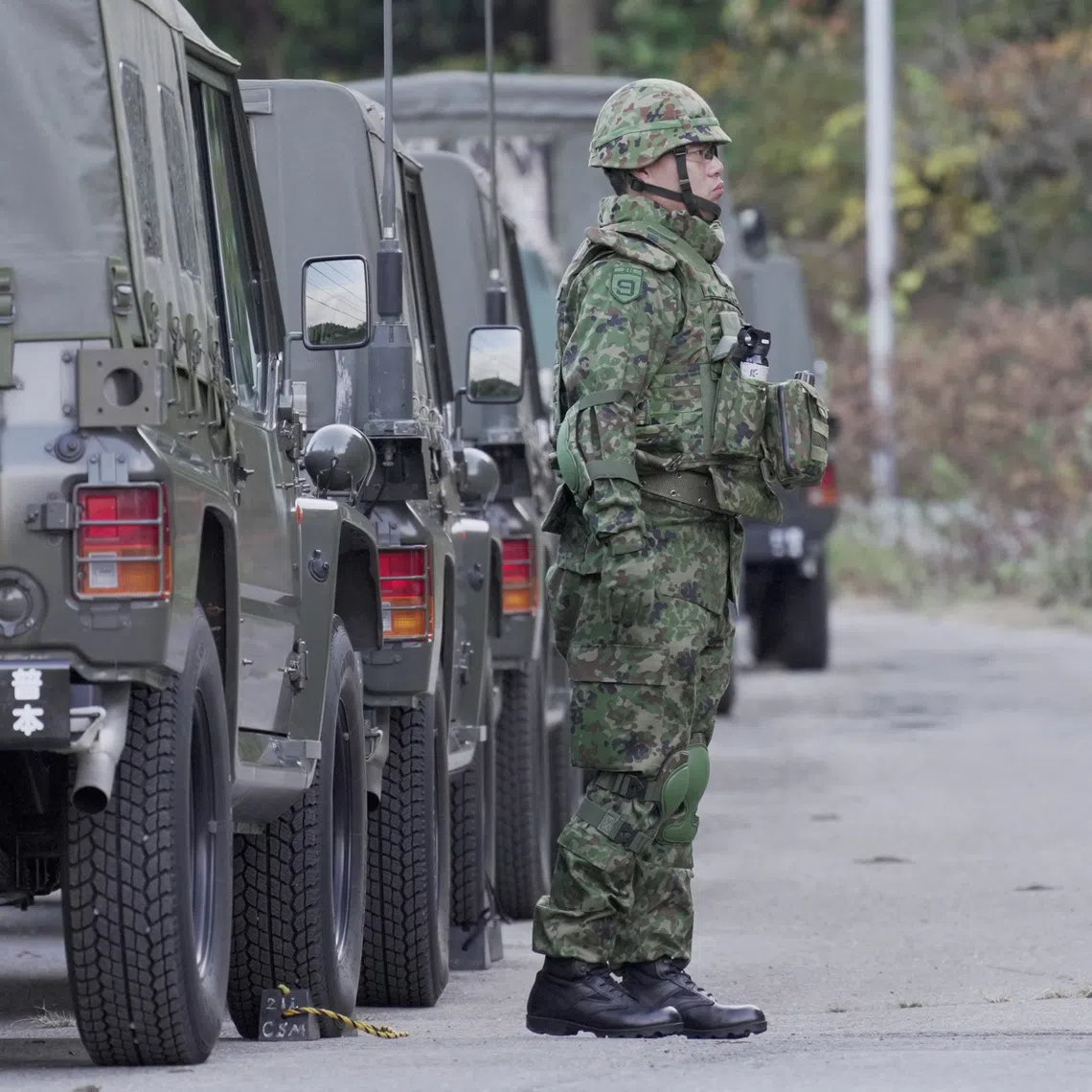 A member of Japan Self-Defence Forces stands next to military vehicles during a practice setting up a bear trap in Kazuno, Akita prefecture, Japan.