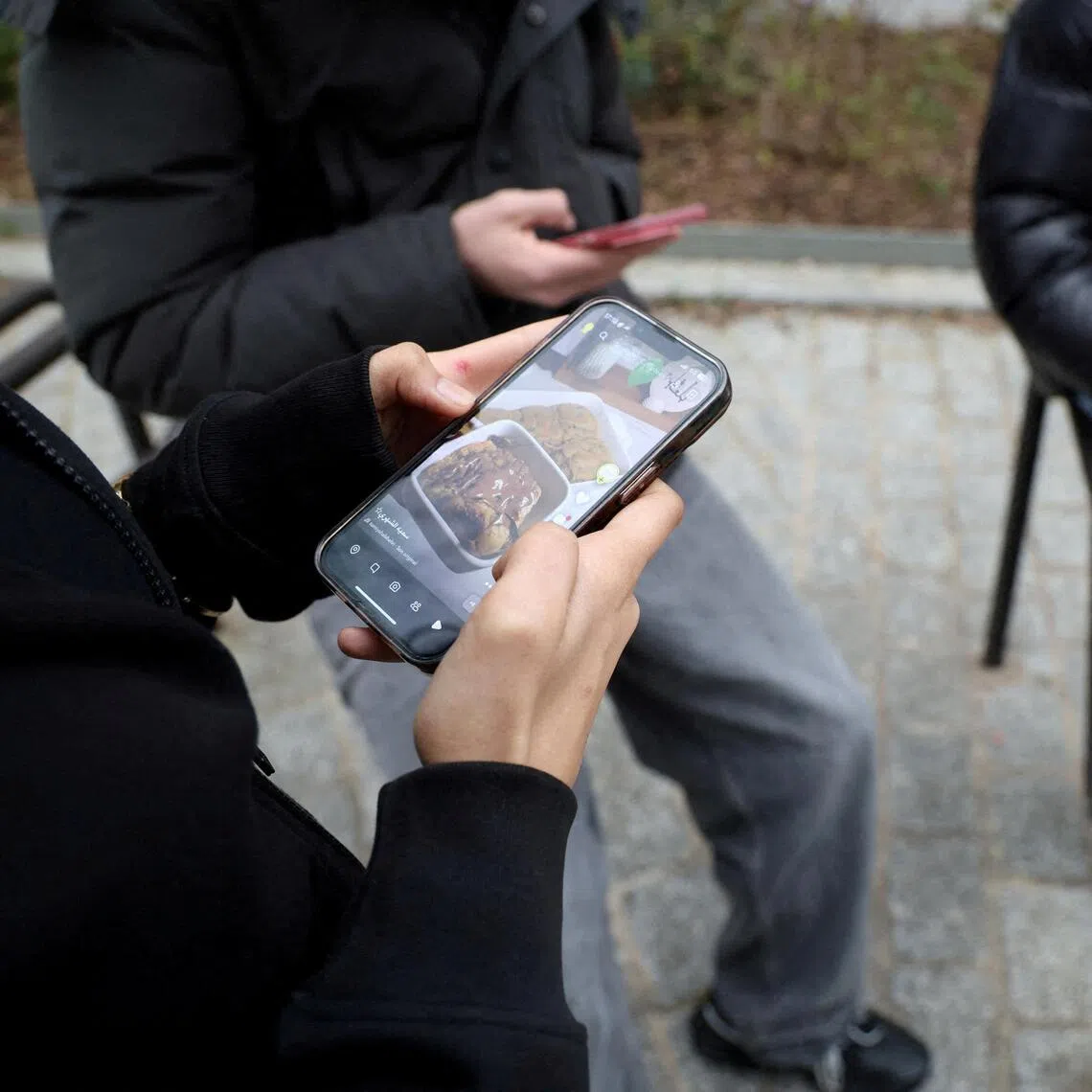 FILE PHOTO: FILE PHOTO: Teenagers look at their mobile phone screens during an interview with Reuters about the bill aimed at banning the use of social networks for those under 15 and mobile phones in high schools from the start of the 2026 school year, in Paris, France, February 20, 2026. REUTERS/Manuel Ausloos/File Photo/File Photo