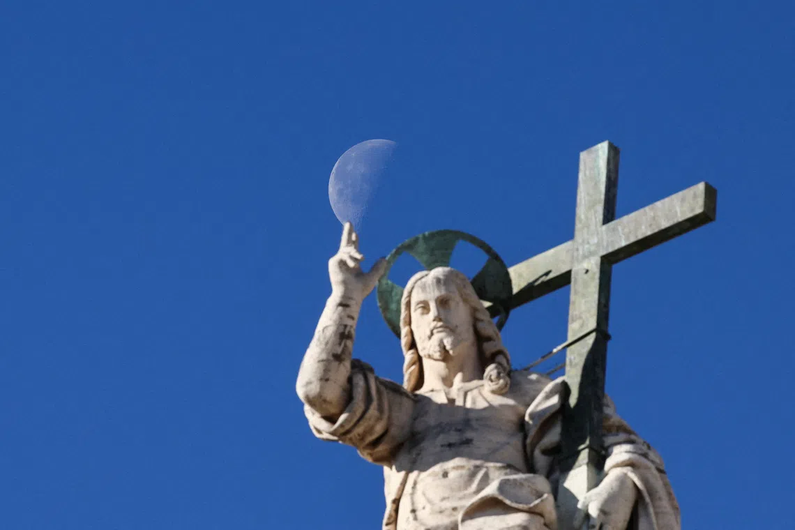 The moon appears in the sky behind the Christ the Redeemer statue on the facade of St. Peter's Basilica, on the day of a general audience in St. Peter's Square at the Vatican, November 12, 2025. REUTERS/Yara Nardi/File Photo