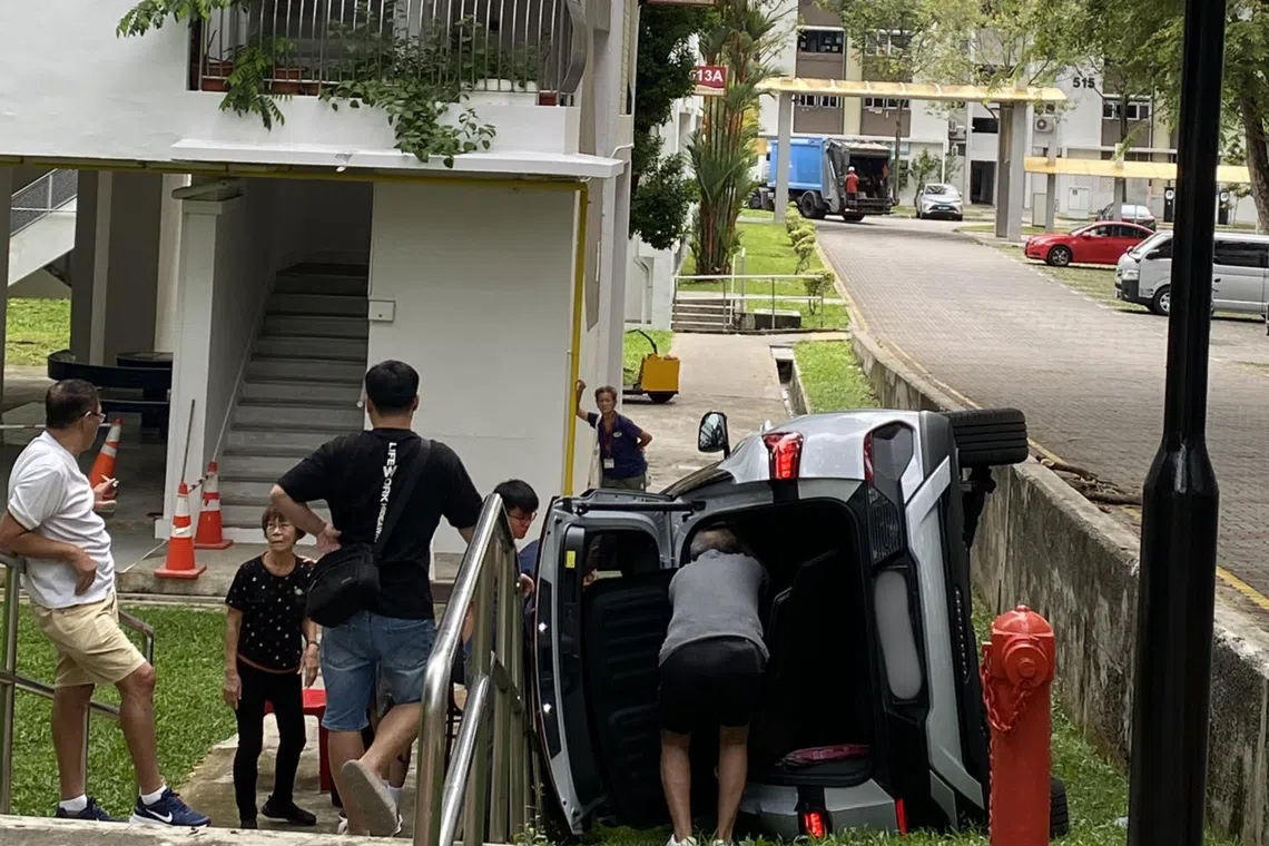 A car is seen on its left side on a patch of grass near Block 514 Bedok North Avenue 2.