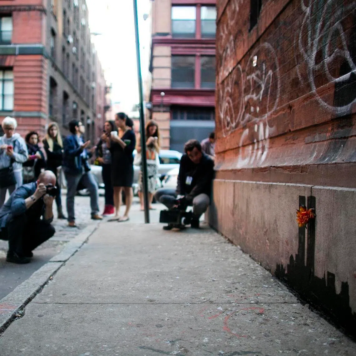 People taking photos of a piece of art by Banksy on a wall in New York on Oct 15, 2013.