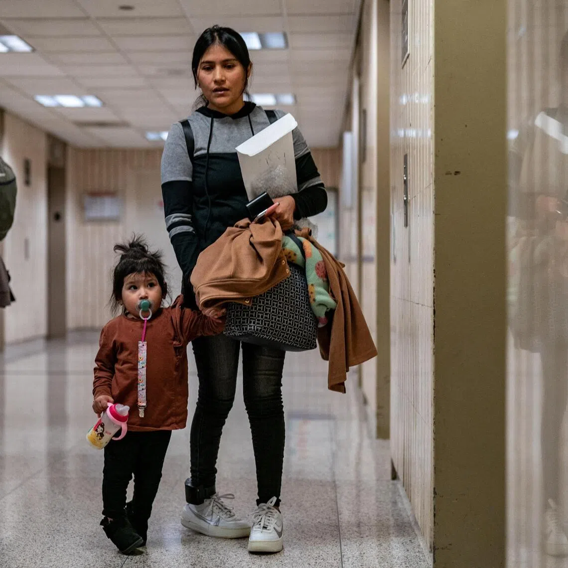 A woman waits with a child at an elevator bank at U.S. immigration court in Manhattan, in New York City, US, on Nov 6, 2025.