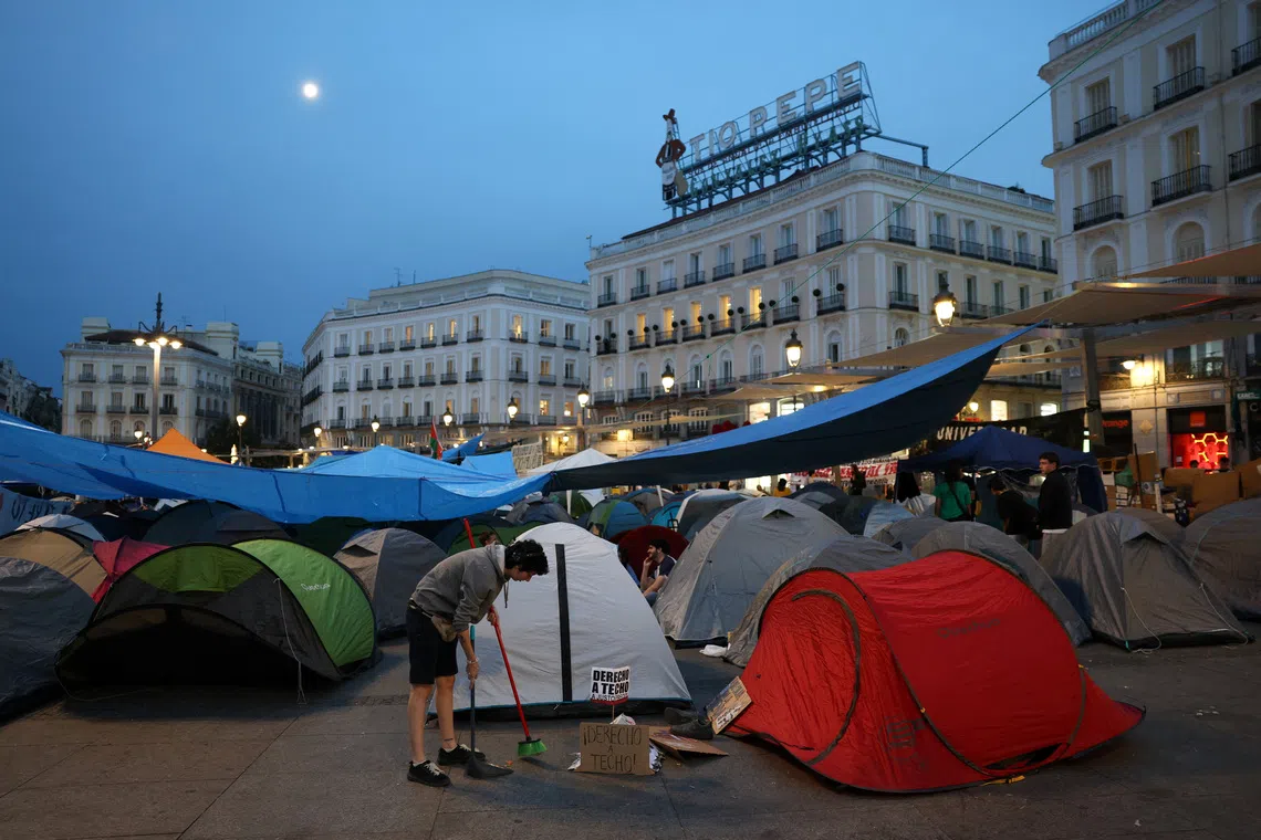 A protester sweeps the pavement next to a sign that reads \"Right to housing\" after demonstrators set up a tent camp at Puerta del Sol square in protest against Spain's housing crisis after the forceful eviction of an 87-year-old woman from her apartment in Madrid, Spain, September 28, 2026. REUTERS/Juan Medina