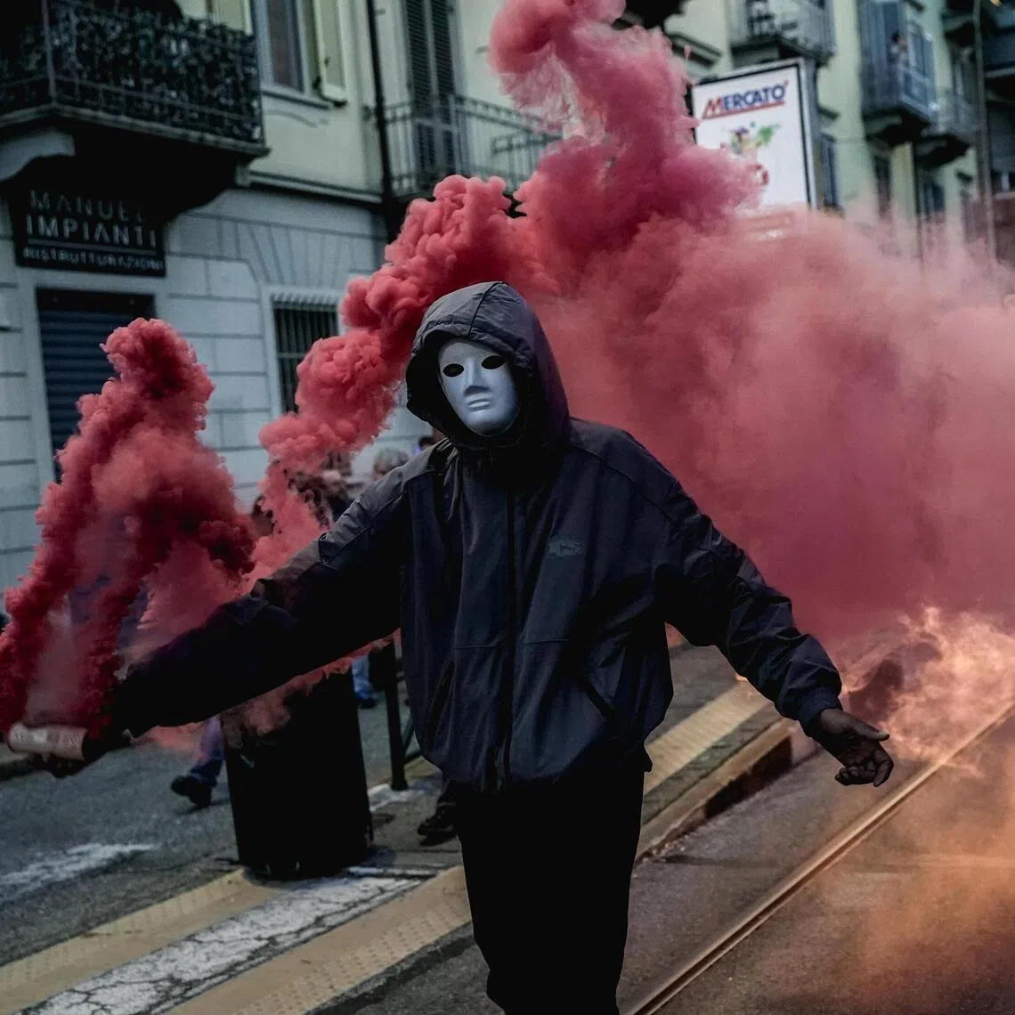 A masked protester holding a smoke flare during a demonstration against rearmament, high fuel prices and data centres in Turin, Italy, on Oct 24.