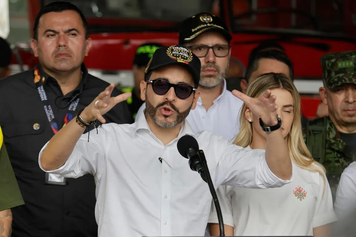 A man in sunglasses and a cap speaks into a microphone while gesturing with his hands, surrounded by a group of people.