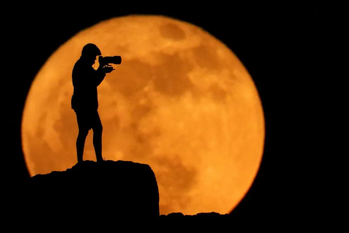 A photographer is silhouetted against the full moon known as the strawberry moon in Arinaga, on the island of Gran Canaria, Spain, June 11, 2025. REUTERS/Borja Suarez      TPX IMAGES OF THE DAY     