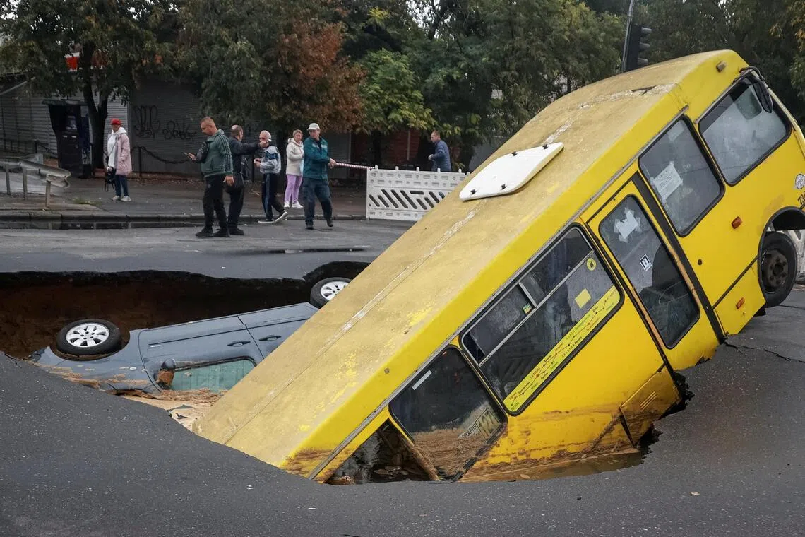Residents in the Ukrainian city of Odesa on Oct 1 walking near a bus and a car stuck in a huge sinkhole that opened up on a road following unprecedented rainfall.  