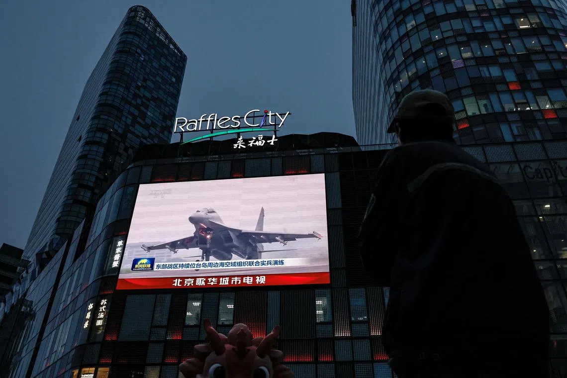 A man looks at a giant screen showing news footage of military drills conducted in areas around the island of Taiwan by the Eastern Theatre Command of the Chinese People's Liberation Army (PLA), in Beijing, China May 24, 2024. REUTERS/Tingshu Wang