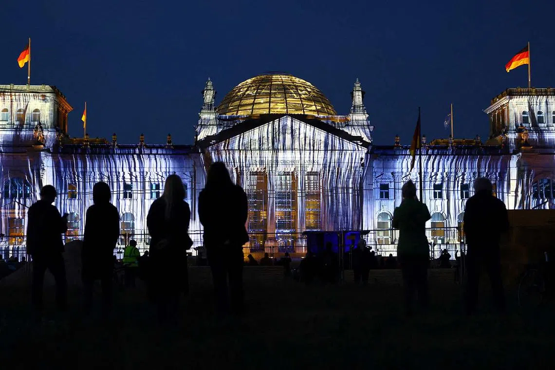Attendees watching a projection onto the facade of the Reichstag building, marking the 30th anniversary of what the Wrapped Reichstag, an installation by artists Christo and Jeanne-Claude, looked like in June 1995, in Berlin, Germany, June 9, 2025. 