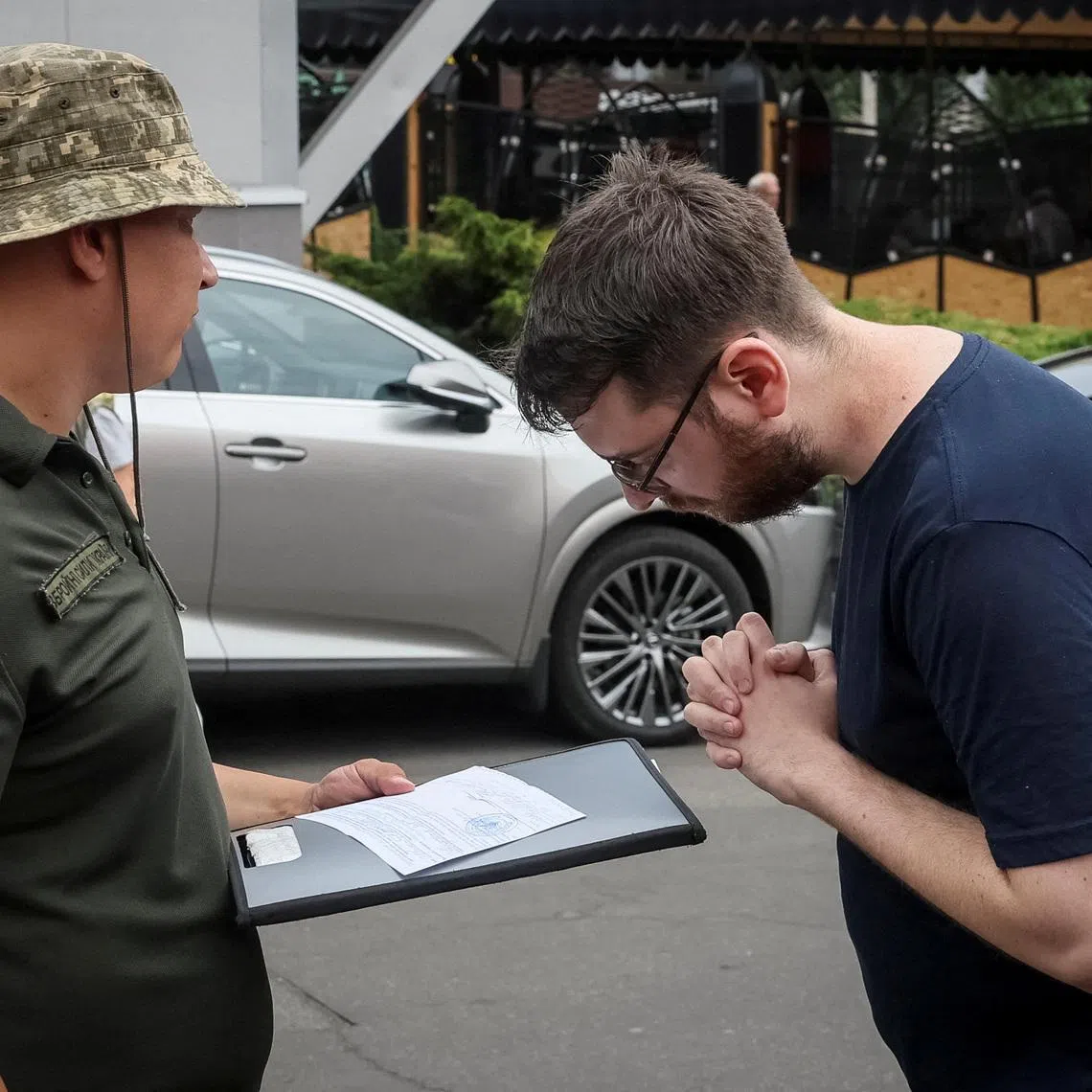 FILE PHOTO: A recruiting officer with the call sign 'Fantomas' speaks with a man on a street as he checks papers of men and hands out military summonses, amid Russia's attack on Ukraine, in Kyiv, Ukraine July 3, 2024. REUTERS/Gleb Garanich/File Photo