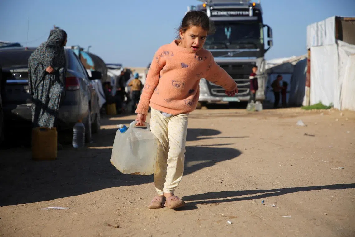 A Palestinian girl carries water she collected from the very few aid convoys that manage to reach Gaza.