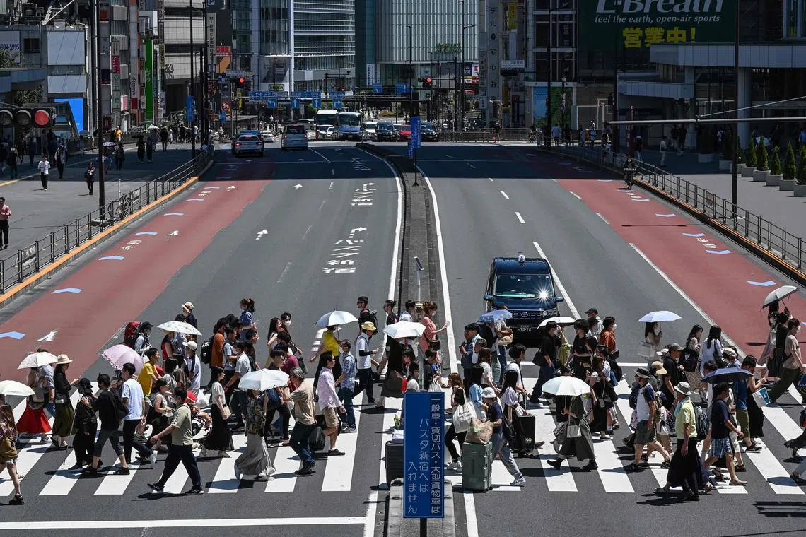 This photo taken on July 30, 2023 shows people using umbrellas and parasols to seek relief from the heat while crossing a street outside Shinjuku station, as temperatures of 35C-plus (95F) have scorched the Japanese capital Tokyo for weeks. Selling jackets with in-built fans, neck coolers and T-shirts that feel cold, Japanese firms are tapping into a growing market for products to help people handle the summer heat. (Photo by Richard A. Brooks / AFP) / To go with AFP story Japan-weather-climate-technology-textile, FEATURE by Elie Guidi and Natsuko Fukue