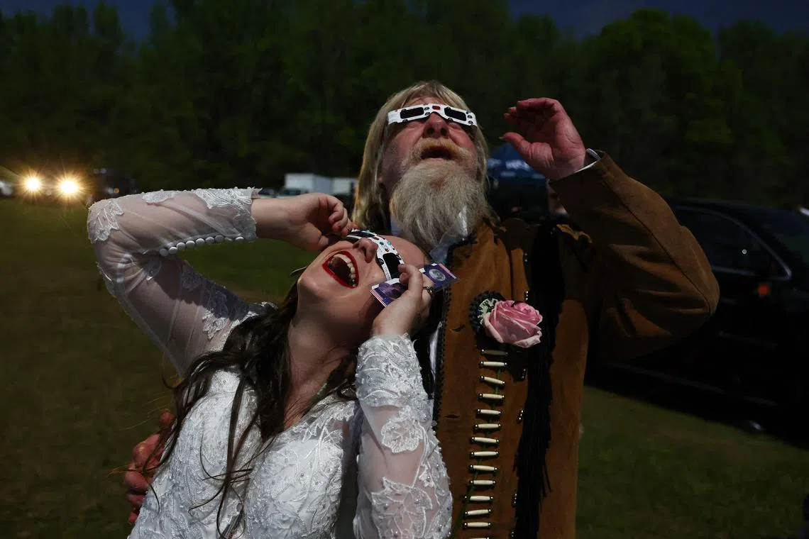 A bride and groom viewing the solar eclipse after marrying at a mass wedding at the Total Eclipse of the Heart festival in Russellville, Arkansas, on April 8, 2024