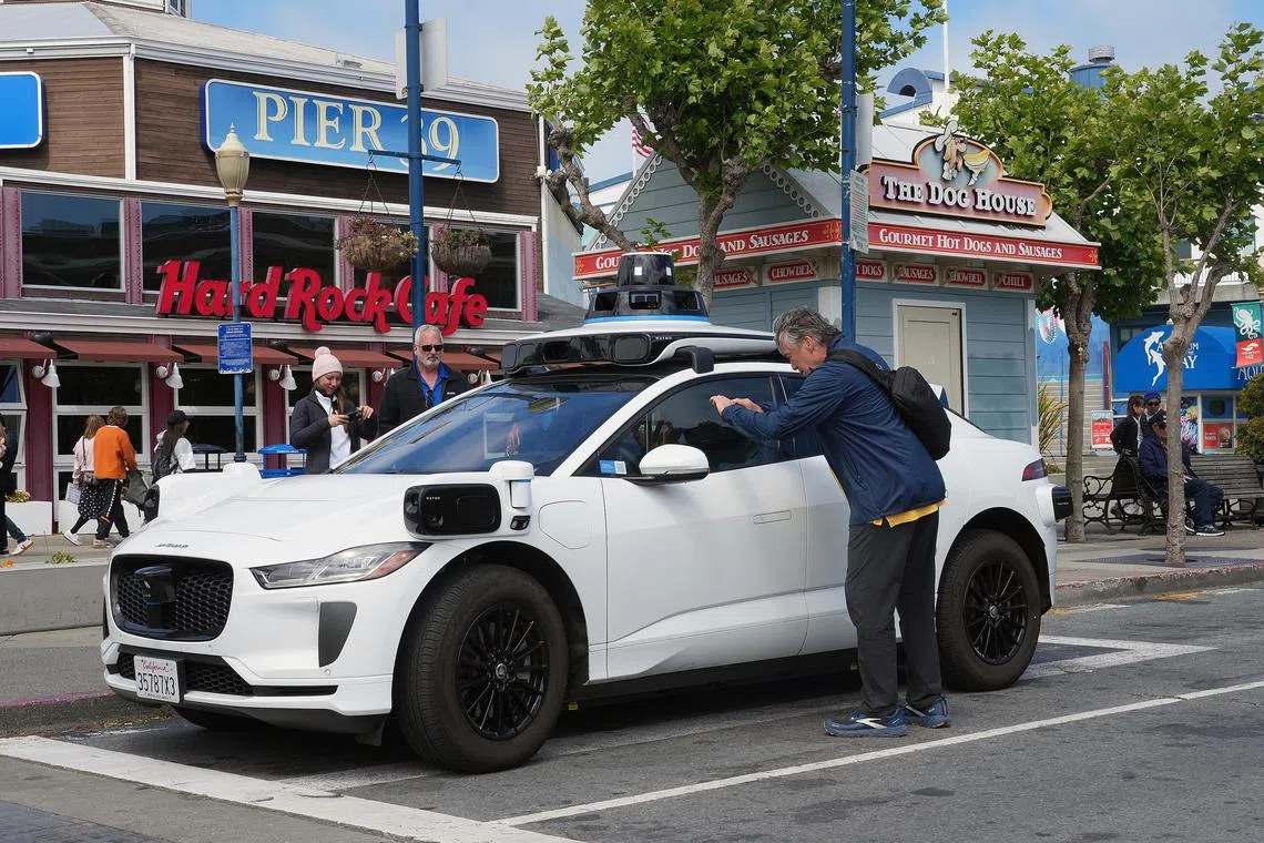 Passers-by stop to photograph a self-driving car from Waymo in San Francisco on May 16. Cable cars are still trundling up the city's hills, but the robotaxis from Waymo are shaping up as the city's latest must-do for visitors. 