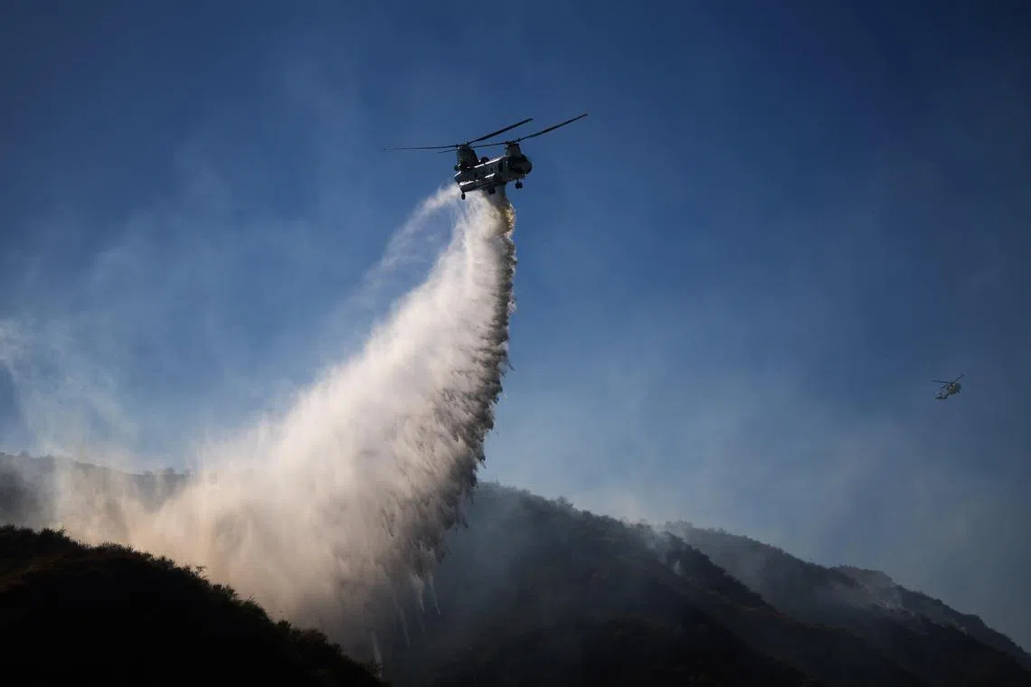 A helicopter drops water as fire crews battle a fire in Simi Valley, California on July 3, 2024.
