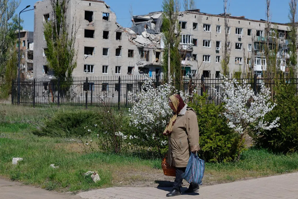 A woman walks from a church during Orthodox Easter celebrations, as an apartment building damaged in the course of Russia-Ukraine conflict is seen in the background, in Avdiivka (Avdeyevka), in the Donetsk region, a Russian-controlled area of Ukraine, April 20, 2025. REUTERS/Alexander Ermochenko