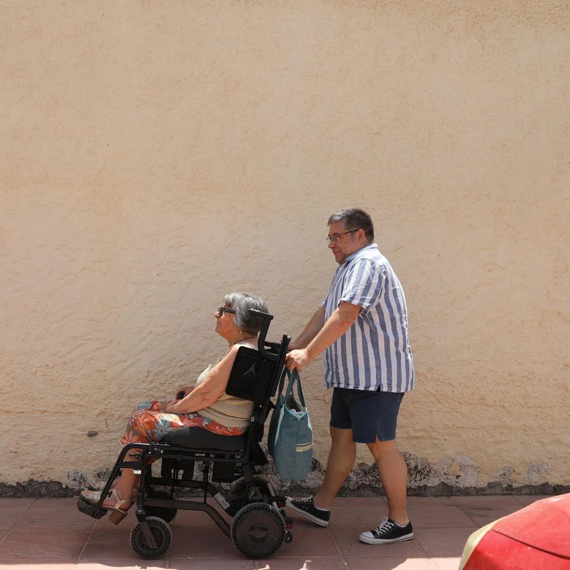 Daniel Northover, 53, who moved from Britain to Spain to care for his mother after her husband's death, takes his mother Carole Bentley, 80, for a walk in her wheelchair along a street in the village of Turre, Almeria, Spain, June 18, 2026. REUTERS/ Loyola Perez de Villegas Muniz