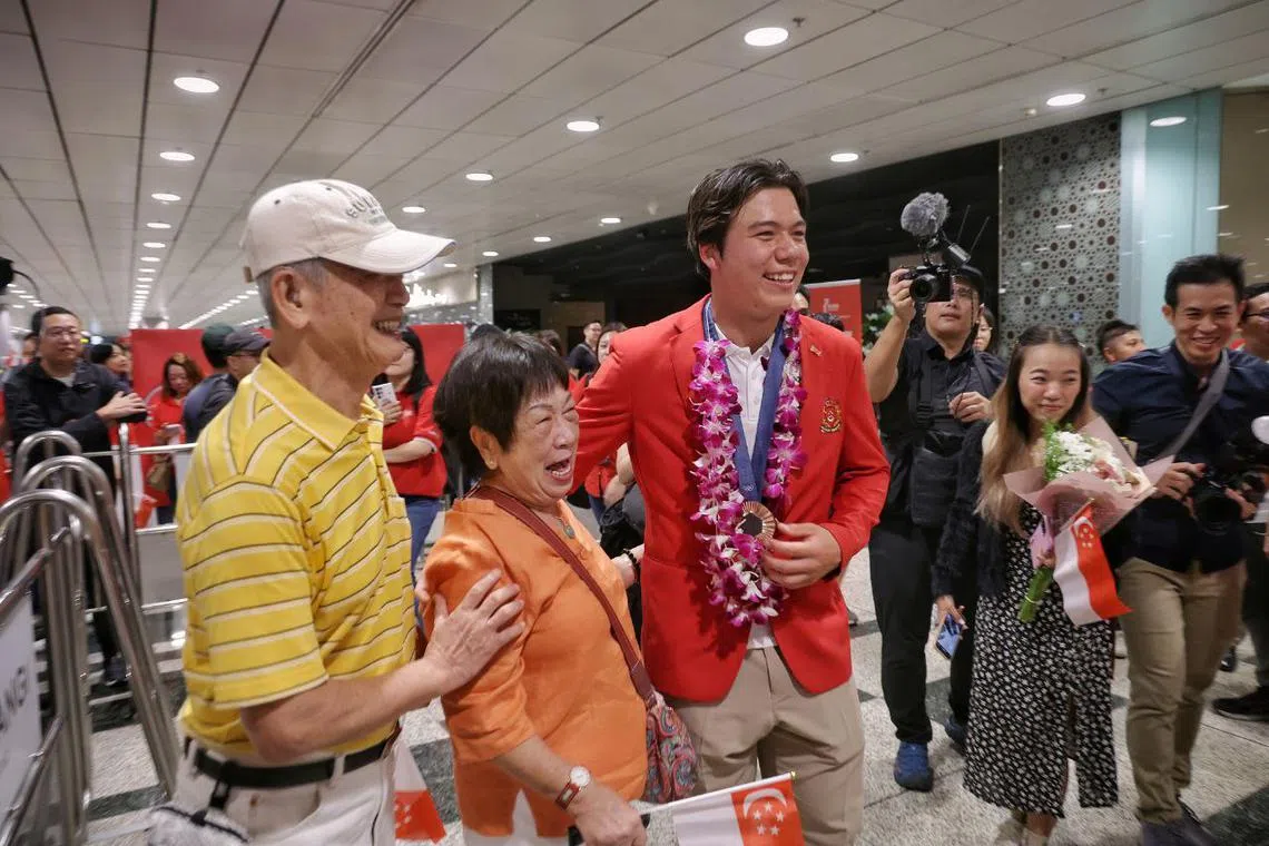 Olympic bronze medalist and kitefoiler Maximilian Maeder sharing a light moment with his grandmother Tan Ah Moy (in orange), 80, and grandfather Teng Lay An (in yellow), 83, at Changi Airport Terminal 3 on Aug 13, 2024. 