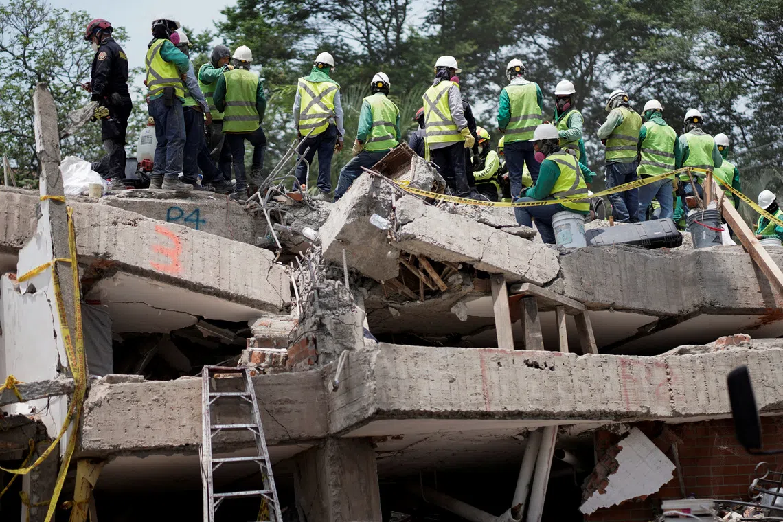 Rescue workers in safety gear standing on the rubble of a collapsed building.