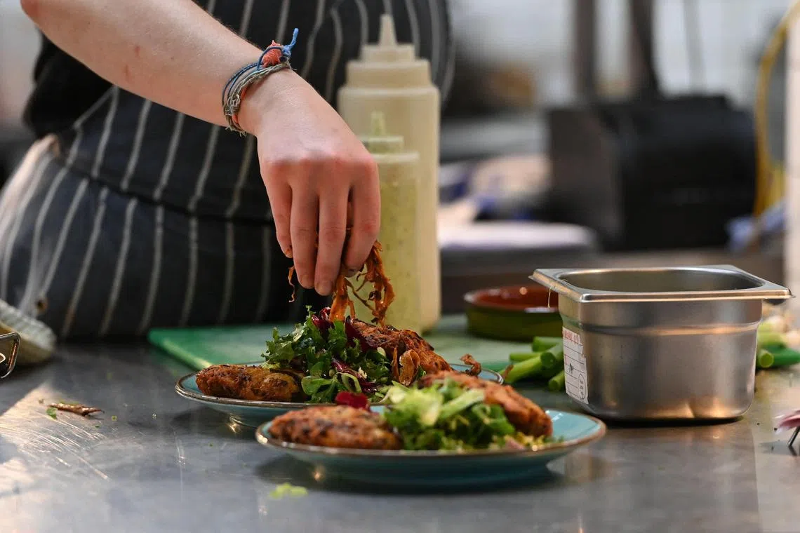A member of staff prepares some food at The Canteen restaurant, one of the first in the UK to place the carbon footprint of its dishes on its menu besides the calories, in Bristol, on August 3, 2022. - The Canteen became in July the first restaurant to agree to put its carbon footprint on the menu under a campaign spearheaded by UK vegan campaigning charity Viva! (Photo by Ashley Crowden / AFP)