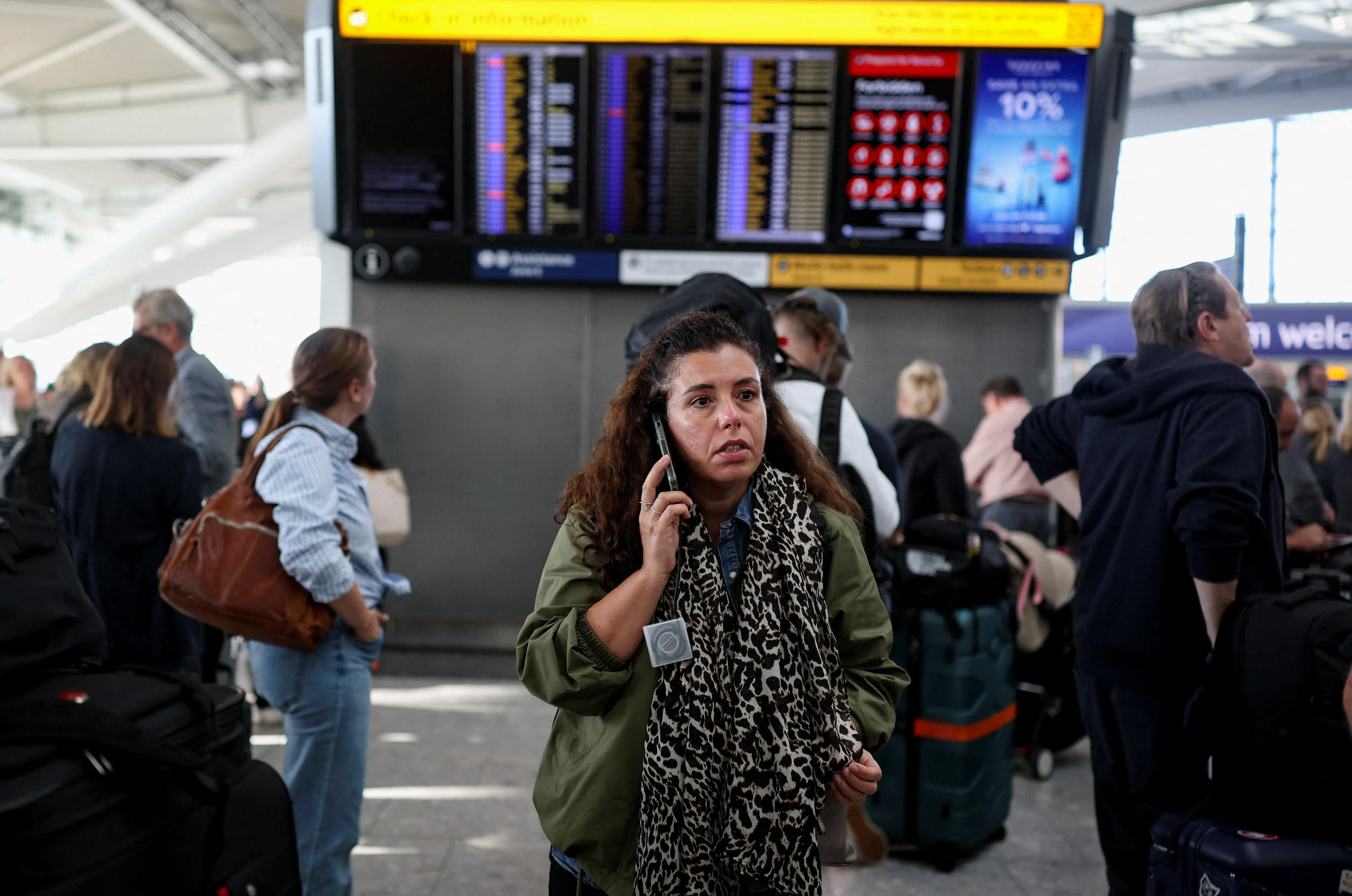 A passenger uses a mobile phone while others look at a departure board displaying cancelled flights at Heathrow Airport's Terminal 5 in London, Britain, September 8, 2026. Some departing flights at major British airports were disrupted on Tuesday after air traffic control provider NATS experienced a technical issue, with Heathrow, Gatwick, Manchester and Stansted among the airports affected by restrictions and delays. REUTERS/Isabel Infantes