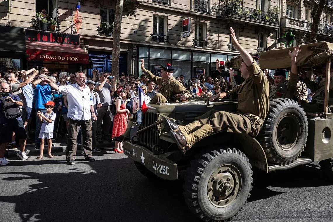 TOPSHOT - Reenactors dressed in wartime uniforms parade on wartime military vehicles during a reenactment marking the 80th anniversary of the liberation of Paris from the Germans during World War II, in Paris on August 25, 2024. (Photo by Olympia DE MAISMONT / AFP)