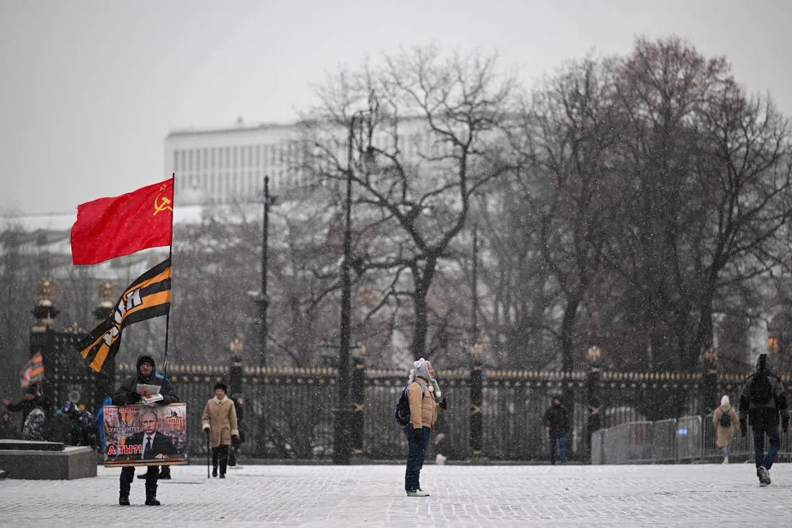 A tourist stands under a light snowfall as an activist holds a single-person picket in support of Russian President Vladimir Putin outside Red Square in downtown Moscow.