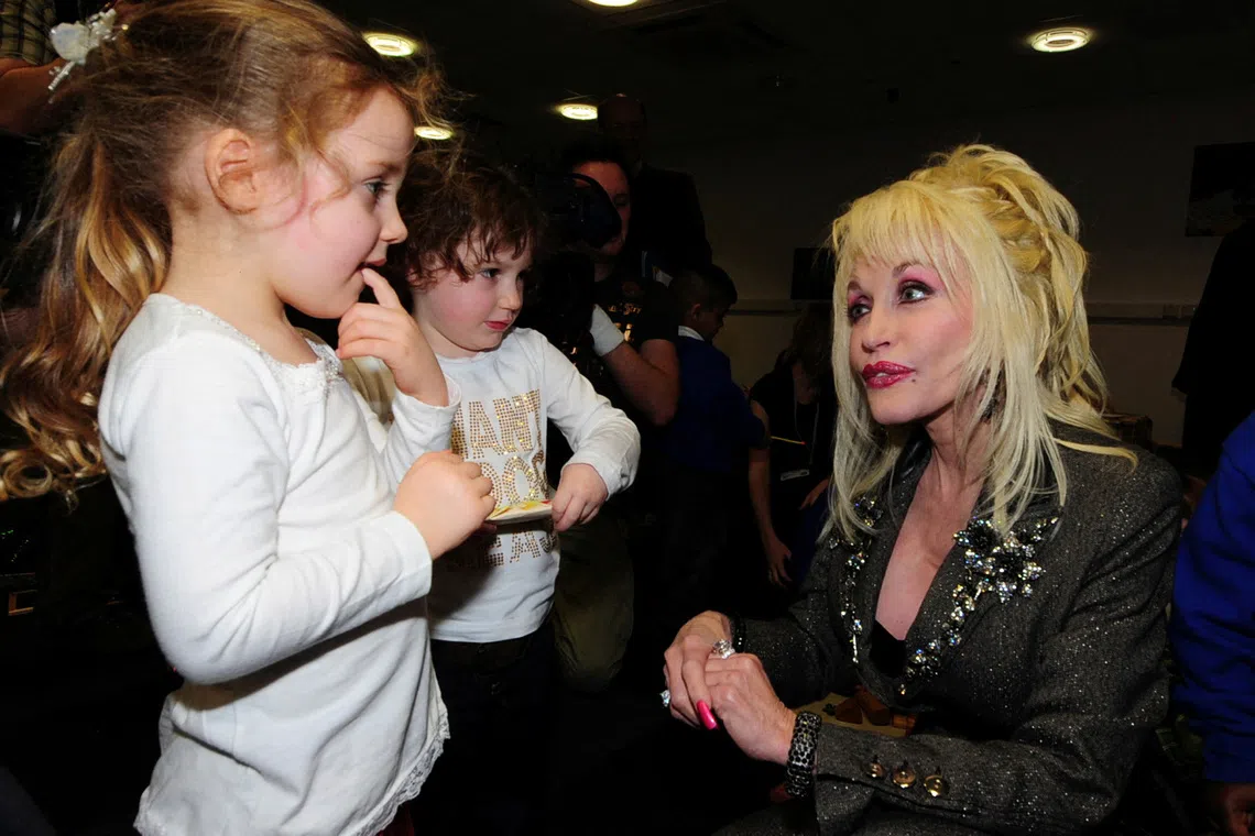 FILE PHOTO: U.S. singer Dolly Parton (R) speaks to children at the launch of her Imagination Library book project  at the Magna Centre in Sheffield in northern England December 5, 2007. Parton's Imagination Library project is an early literacy programme for children. REUTERS/Nigel Roddis/File Photo
