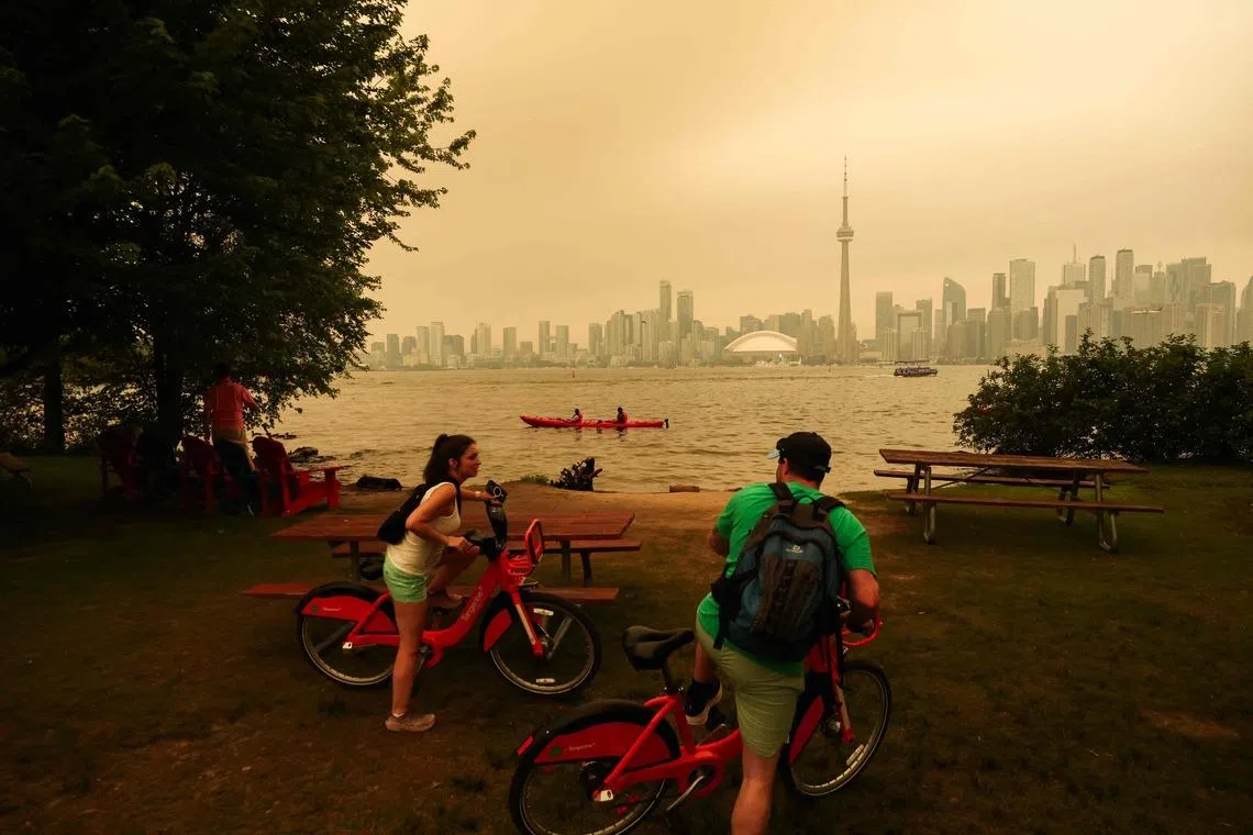 TOPSHOT - People pause as they cycle on the Toronto Islands as forest fires in Northern Ontario cause poor air quality over the city, in Toronto, Ontario, Canada, July 15, 2026. Toronto had the worst air quality of any major city in the world on Wednesday, the Swiss firm IQAir said, as Canadian authorities urged people to stay indoors. Toronto edged out New Delhi and the Democratic Republic of Congo's capital Kinshasa as wildfire smoke turned the skies a hazy yellowish-grey in Canada's largest city. (Photo by Cole BURSTON / AFP)