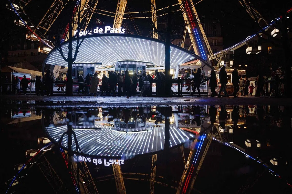 Visitors walking past the entrance to the ferris wheel at the seasonal Christmas market and fairground in the Jardin des Tuileries gardens in central Paris, on Nov 24, 2025. 