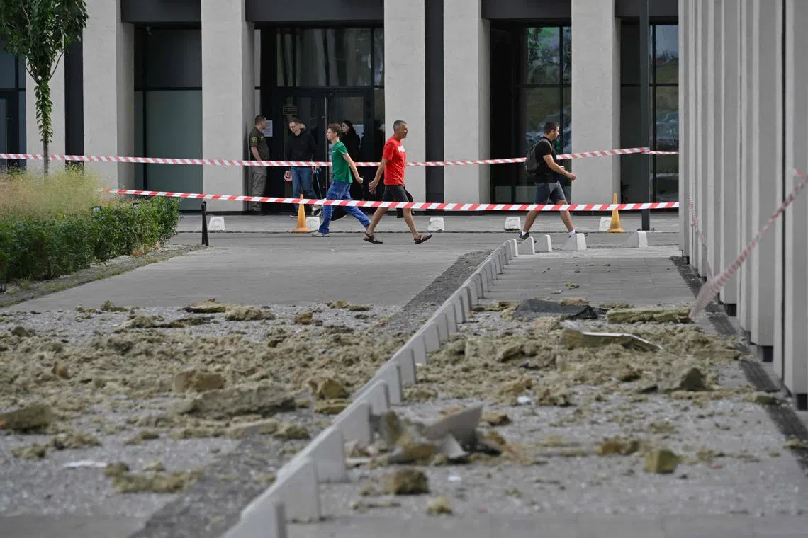 People walk past a high-rise residential building damaged by the remains of a Russian drone shot down over Kyiv.